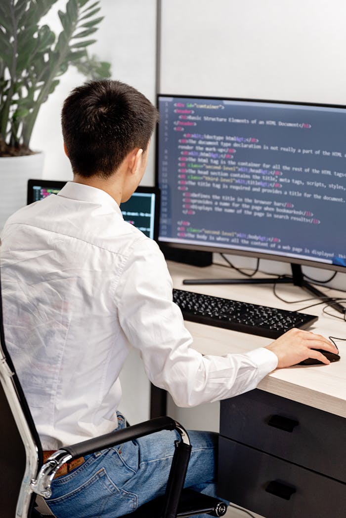 home-img Back view of a programmer in a white shirt coding in an office workspace.